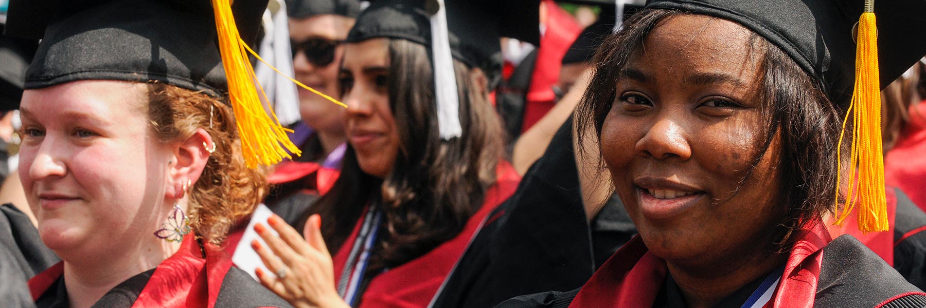 A woman in graduation attire smiles for the camera amongst a crowd