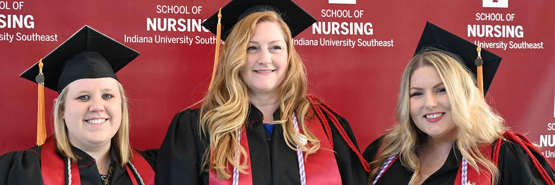 Three smiling IU Southeast nursing school graduates wearing robes and caps